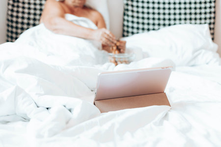 Blond woman with tablet computer in bed at home, watching movies and Internet. Eat grapes fruit....