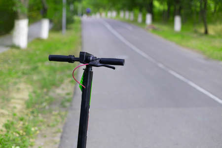 Black electric scooter transport is parked along the road of the park on summer day. Public scooters are available to rent as a means of transportationの写真素材