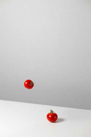 Fresh cherry tomatoes fly in the air. Stylish trendy creative art composition on white table background. Levitation of fresh cut tomato. Vertical orientationの写真素材