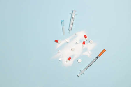 White pills, colored capsules and syringes with a needle on a light blue pastel table. International day against drug abuse. Top view, flat lay. Medical banner design templateの写真素材