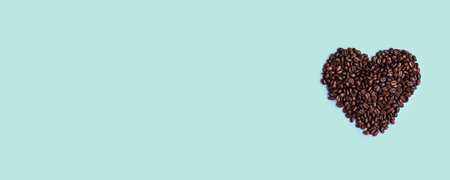 Freshly roasted heart shaped brown coffee beans with copyspace on a mint solid color background,top...