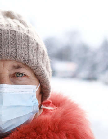 Caucasian woman wearing medical mask looking to the camera at street of city in winter time. Safety in public place during virus outbreak.の写真素材