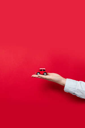 Female hand holding toy red model car on red background. Car insurance concept, copy spaceの写真素材