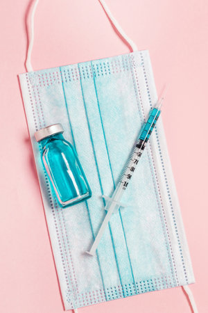 Syringe with medicine from a glass bottleab a protective medical mask on pink background.の写真素材