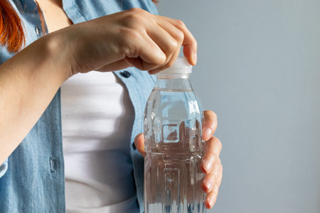 Woman hand opening water bottle on a gray background. Drinking mineral water from bottle