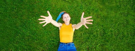 Joyful and smiling girl lies on the grass looks at the camera outside in park