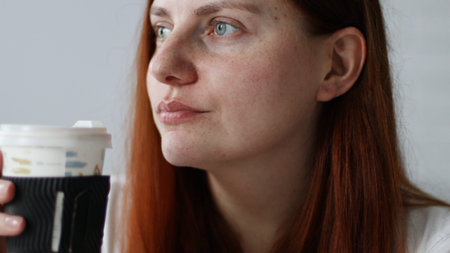 woman drinking coffee from paper cup sitting on couch at home at morning