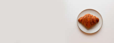 Freshly baked croissant with caramel filling on plate on grey background. Minimal composition. Flat lay, top viewの写真素材