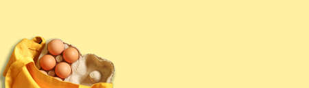 Brown chicken eggs in an open carton box in shop bag on yellow backgroundの写真素材