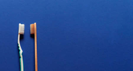 Two plastic and natural bamboo toothbrushes on blue background with copy space. People teeth hygiene.の写真素材