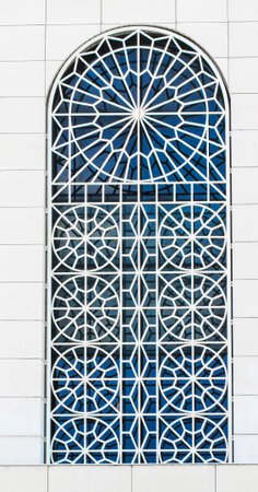 One large gray old window with ornamental metal lattice of building wall