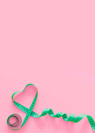 Green plastic measure tape in the shape of a heart with metric scale over on color background. Fitness concept. Top view, copy spaceの写真素材