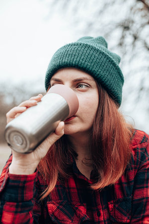 Caucasian woman drinks from a mug of flask. Rest at in nature autumn forest