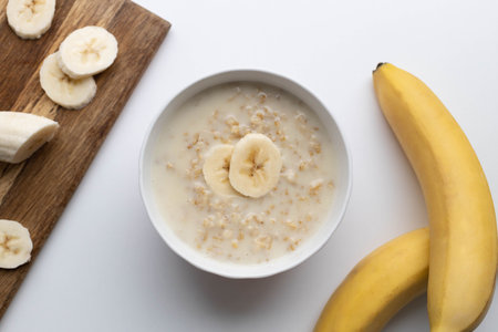 Bowl of oatmeal porridge with banana on white table for healthy breakfastの写真素材
