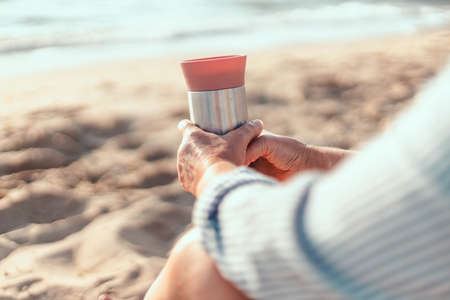 Woman with mug of coffee by autumn sea. Morning picnic with thermos of hot tea or coffee on beach. Girl is enjoying nature, life, relaxation.の写真素材