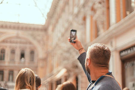 Back close up view of a young man takes pictures of the architecture of a building or landmarks on his phone.の写真素材
