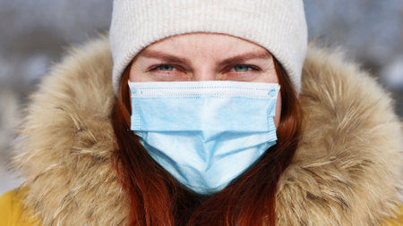Close up portrait face of young girl in protective medical mask looking at camera in winter time.の写真素材