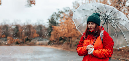 Beautiful girl holding a transparent umbrella during the rain in the autumn cloudy weather in the...