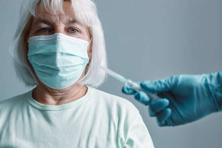 Vaccination, immunization campaign, disease prevention concept. Young woman in medical face mask getting Covid-19 vaccine at doctors office. Professional nurse giving flu injection to patientの写真素材