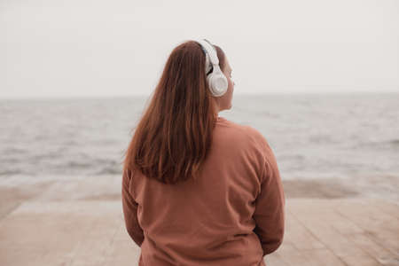 Relaxed cute girl listening to music on the beach at sea backgroundの写真素材