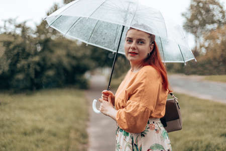 Beautiful long-haired girl with a transparent umbrella enjoying the rainy weather.の写真素材