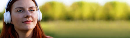 Happy young girl student listening music with headphones sitting outdoors in beautiful green parkの写真素材