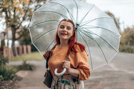 Stylish young woman in bright clothes under a transparent umbrella in bad weather.の写真素材