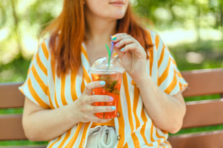 Summer beautiful happy woman hands holding refreshing aperol spritz cocktail at the city park....