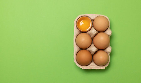 Brown chicken eggs and one broken egg with yolk on green background