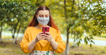 Happy woman walking using mobile phone wearing face mask protection as prevention for virus in city...
