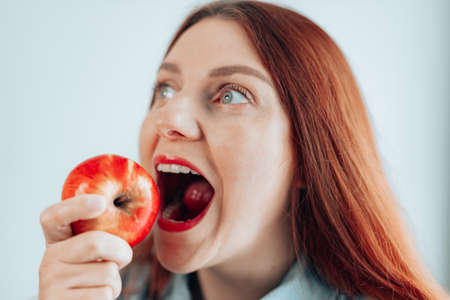Portrait of a cheerful young woman eating red apple on gray wall background. Healthy nutrition diet. Apple vitamin snack.の写真素材