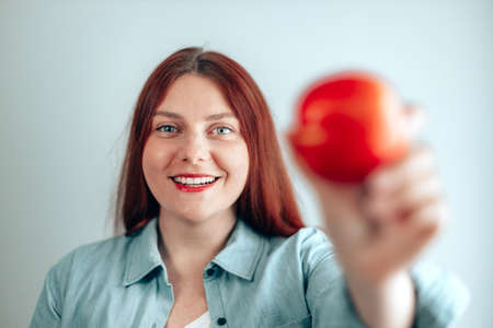 Portrait of a cheerful young woman eating red apple on gray wall background. Healthy nutrition diet. Apple vitamin snack.の写真素材