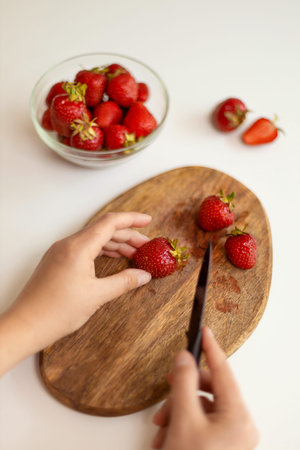Womans hand cuts strawberries with a kitchen knife