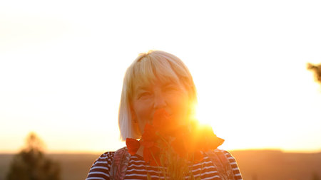 Caucasian woman tourist with backpack and poppy flower bouquet at sunset in the field. Summer...