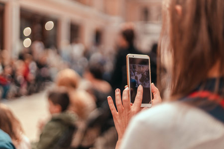Woman taking pictures using smartphone or filming video of models on catwalk