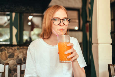 Portrait of excited happy lady drinking healthy orange juice smoothie in city street cafeの写真素材