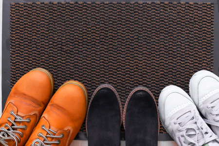 Female brown suede and black boots on a black welcome sign carpet.