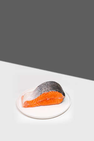 Single fresh raw salmon steak on the edge of white table. Creative mockup with copy spaceの写真素材
