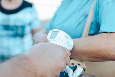 Person measures temperature with digital medical infrared forehead thermometer non contact for measuring temperature, for coronavirus COVID-19 testing during an epidemic outdoors.の写真素材