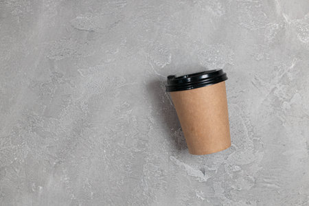 Blank take away coffee paper cup isolated on a gray concrete background.
