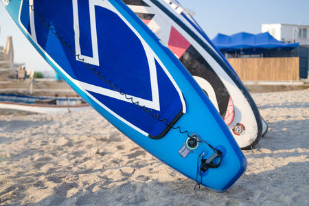 Group of blue SUP stand up paddle boards on the beach sand for tourist rent. Surfing boards on stand...
