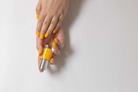 Bright yellow manicure with a bottle of nail polish in hands on gray background. Flat lay style.の写真素材