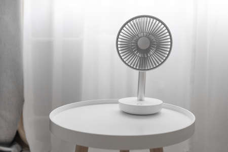 Modern electric portable fan on a white coffee table in bedroom. Cooling of high air temperature. Minimal style, copy space.の写真素材