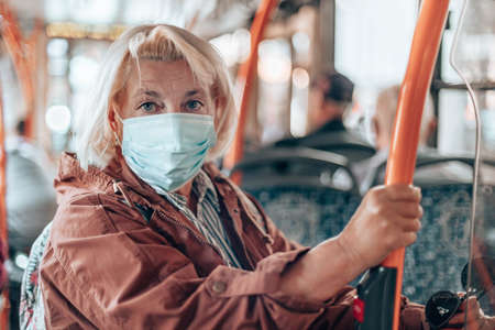 Adult 40-50 year old female passenger wearing a surgical mask on a subway train or bus transport while traveling in city during Covid 19の写真素材