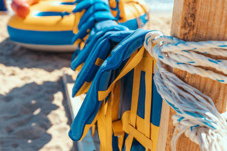 Emergency rescue equipment important for life security in the water or the sea. Many colorful yellow blue marine life vest signal jackets or life vest hanging on the beachの写真素材