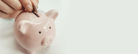 Save money concept. Close up of woman putting a coin inside piggy bank as investmentの写真素材