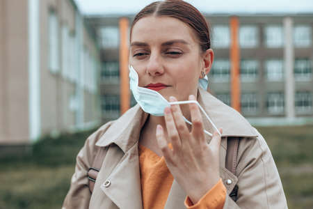 Caucasian woman taking off protective medical mask in city park. We won. No more quarantine.の写真素材