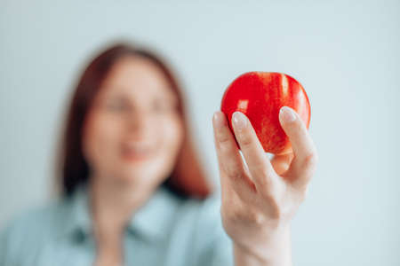 Cheerful young woman eating red apple on gray wall background. Healthy nutrition diet. Apple vitamin snack.の写真素材