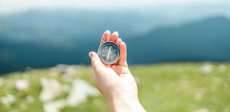Traveler holding compass in hand for discover direction on the background of hills and the sky with clouds. Vacation and travel. Carpathians, Ukraineの写真素材