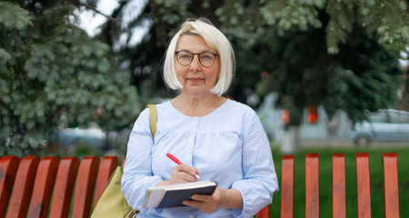 Beautiful adult 35-40 years old businesswoman in a park holding a notebook and pen outdoors in a city park in summer outdoorsの写真素材